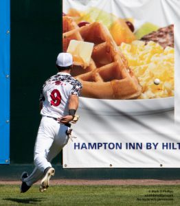 Nashua Silver Knights center fielder Ben Rounds, a sophmore at Harvard, chases the ball into a breakfast photo on a drive to the wall during FCBL game with the North Shore Navigators at Holman Stadium in Nashua, NH. ©Mark D Phillips