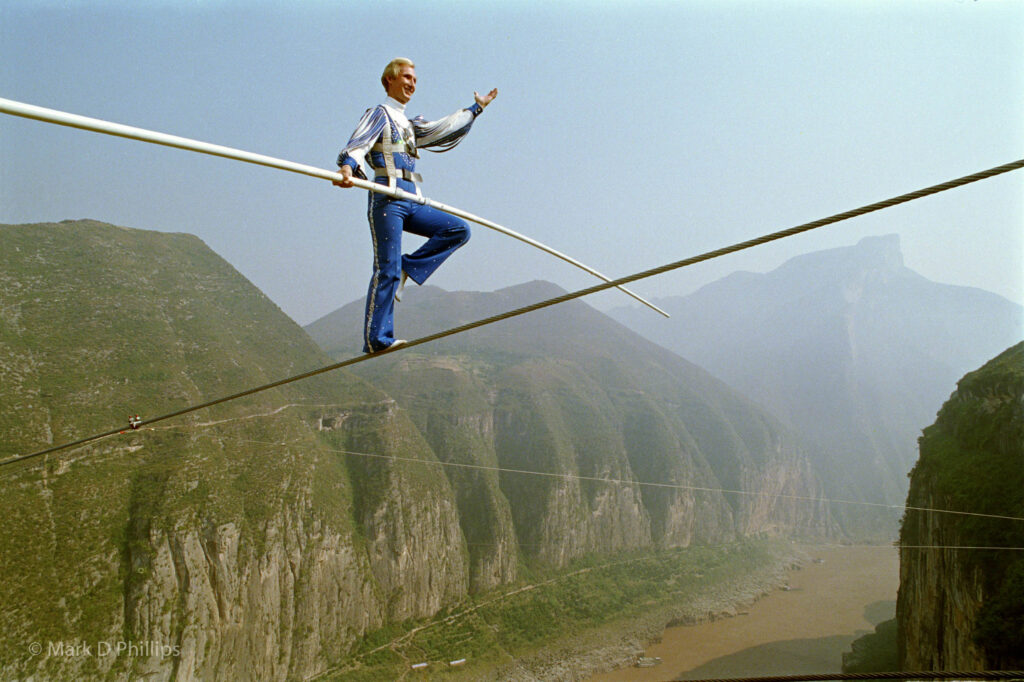 Jay Cochrane salutes his audience during The Great China Skywalk over the Yangtze River in Qutang Gorge, China, on October 28, 1995. The skywalk was and is the greatest ever made spanning half a mile between the canyon walls and 1,350 feet above the river. Photo by Mark D Phillips