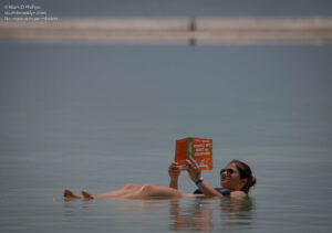Emily Hametz reads "People We Meet on Vacation" as she floats in the water of the Dead Sea. ©Mark D Phillips
